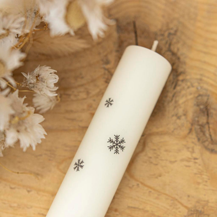Stabkerze mit Schneeflocken als Detailaufnahme auf einer Stabkerze in Creme