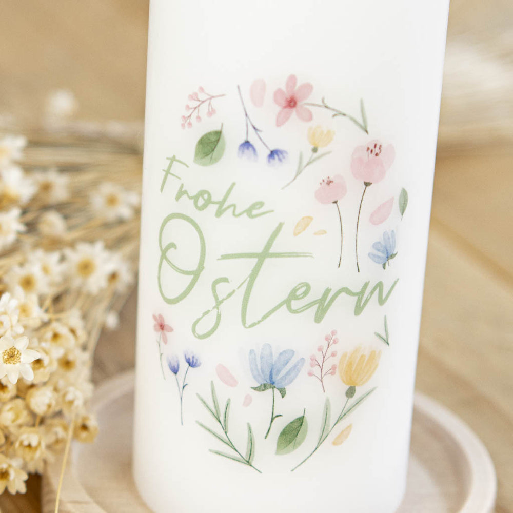 Osterkerze mit Blumen und dem Gruß Frohe Ostern