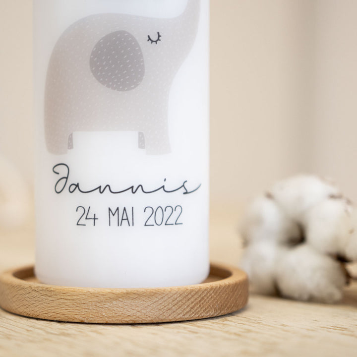 personalisierte Taufkerze mit einem Elefanten steht auf einem Kerezenhalter aus Holz